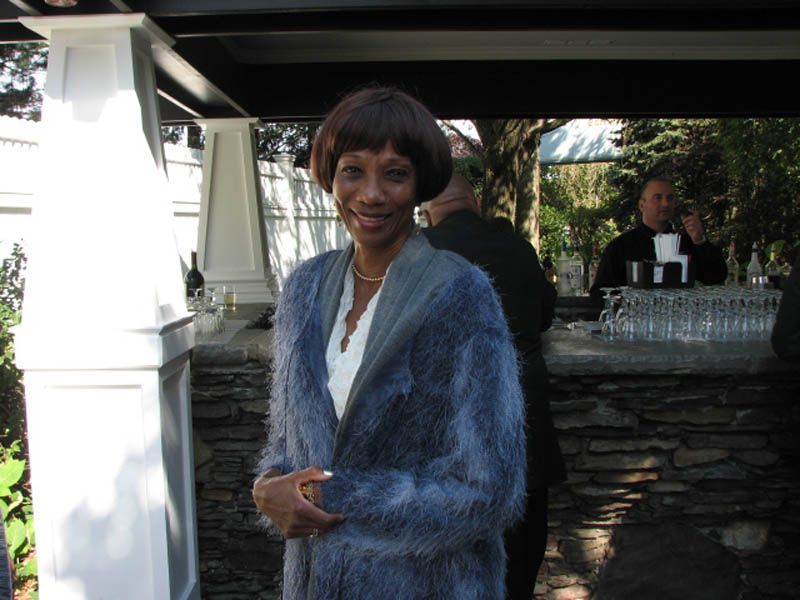 Woman in a blue fuzzy coat, standing near a bar at an outdoor event.
