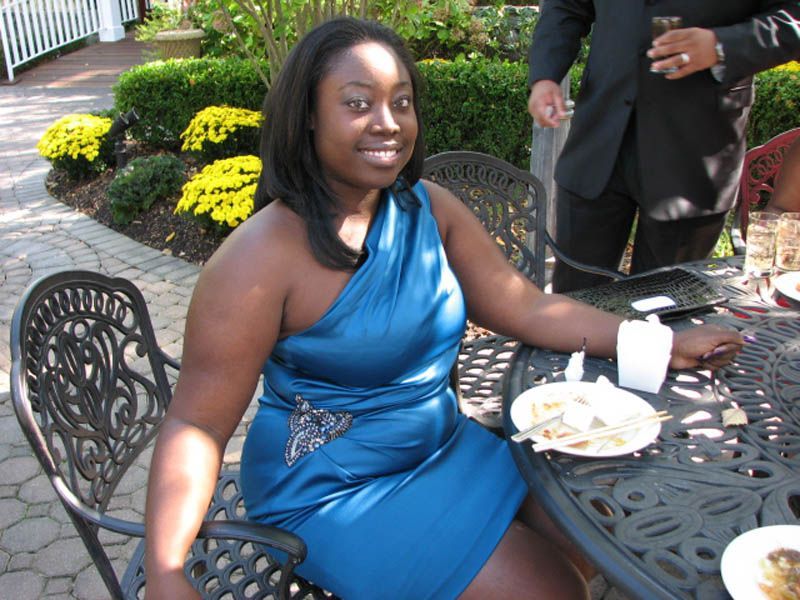 Woman in blue dress sits at outdoor table, smiling.