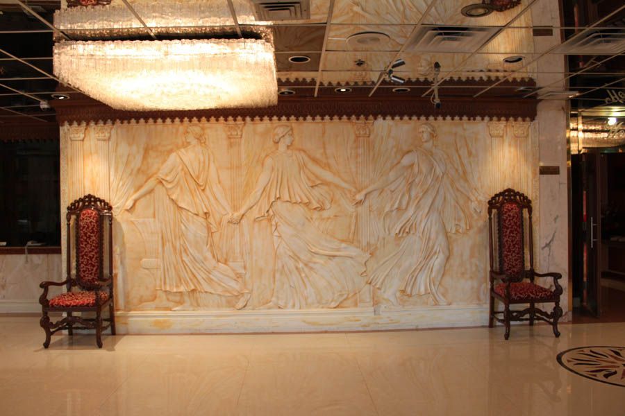 Wall relief of figures dancing, flanked by ornate chairs. Large chandelier overhead.