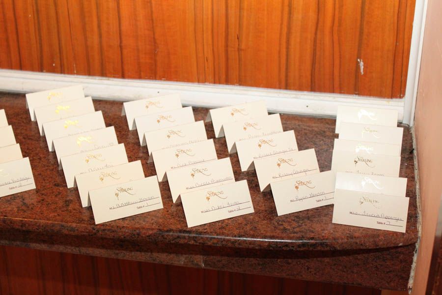 A display of rectangular place cards with gold script on a brown surface against a wooden backdrop.
