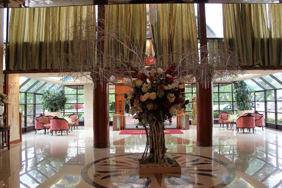 Lobby with floral arrangement, seating areas, and large windows. Beige, pink, and reflective surfaces are prominent.