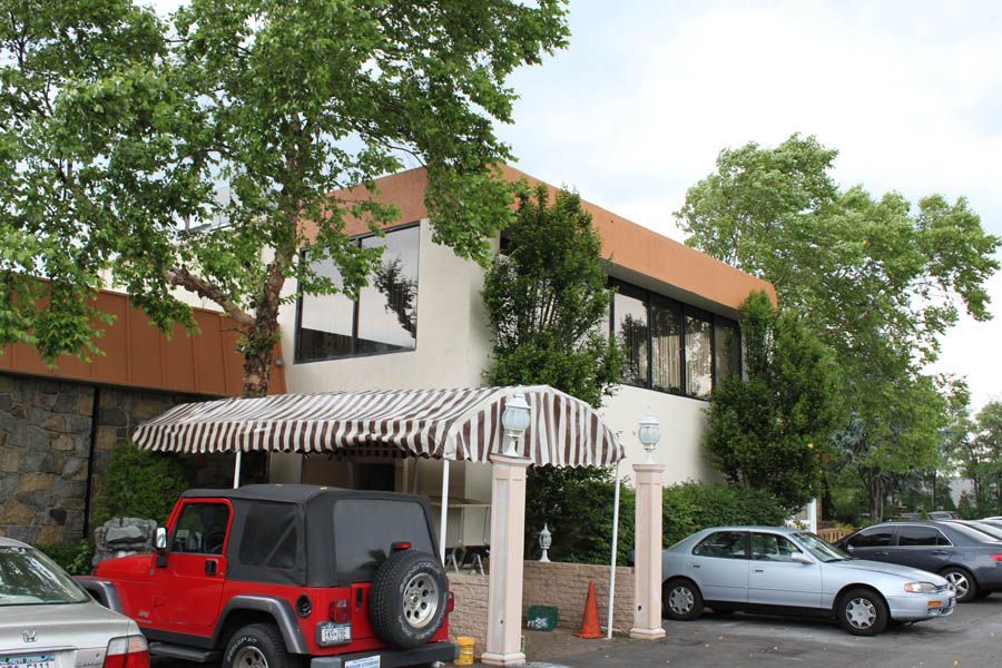 A building with a striped awning, pillars, and a red jeep parked in front.
