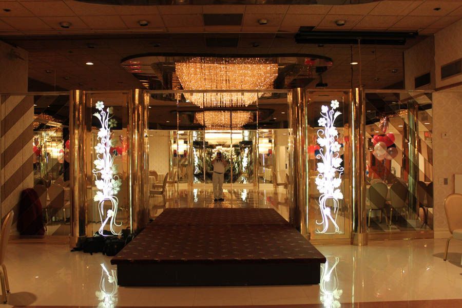 A room with a stage, gold accents, and a large chandelier. A person stands in the distance.