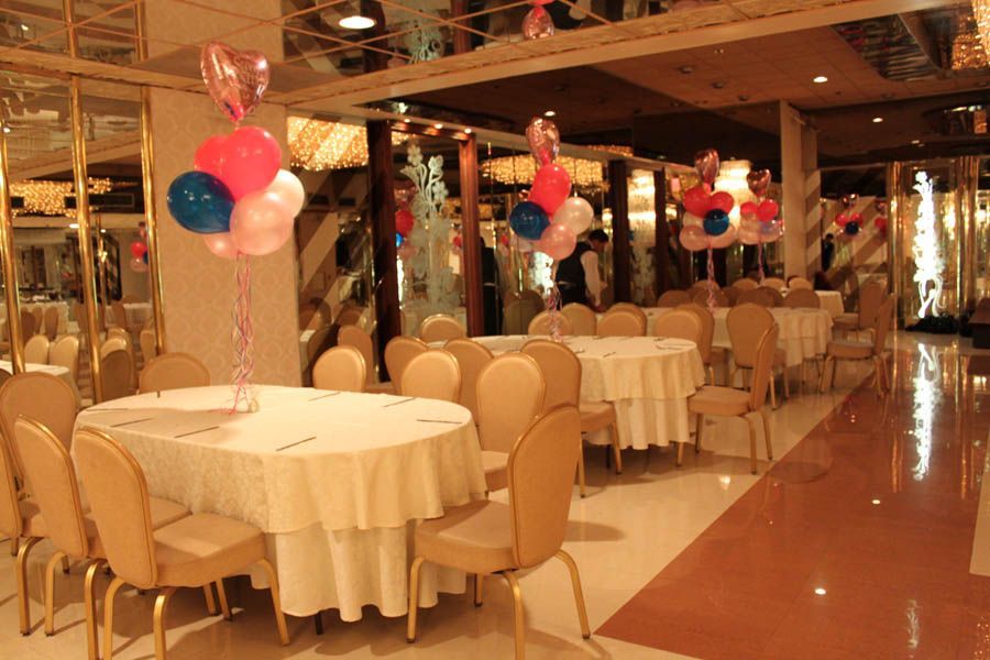 Restaurant with round tables set for a party, decorated with balloons. Gold and pink decor.