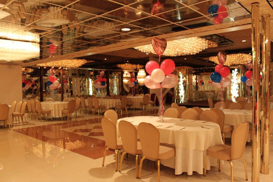 Banquet hall with round tables, balloons, mirrored ceiling, and gold accents.