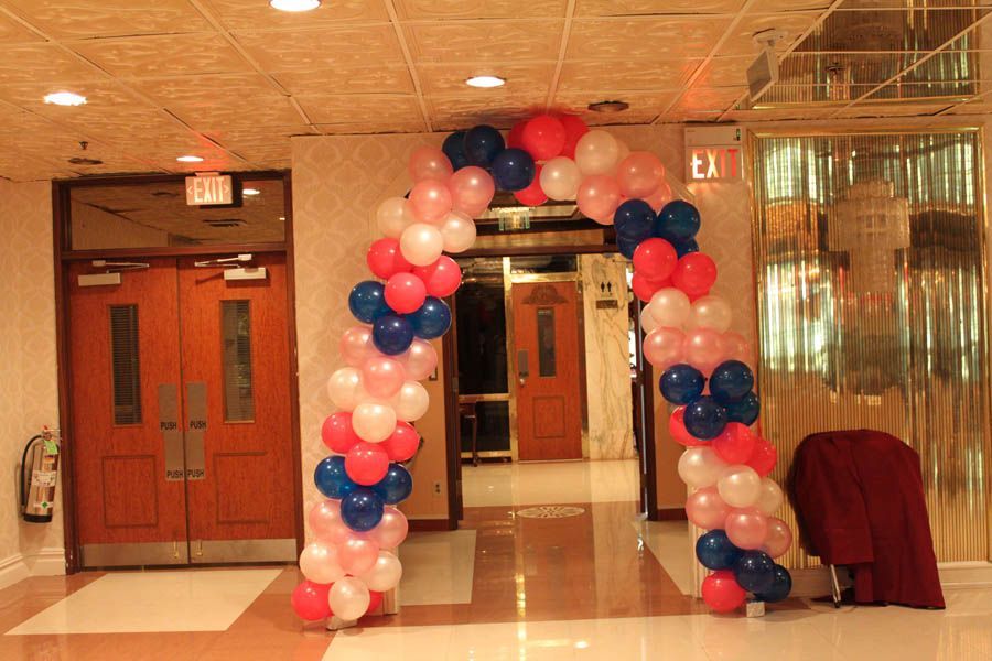 Balloon arch in red, white, and blue colors frames a doorway in a building's hallway.