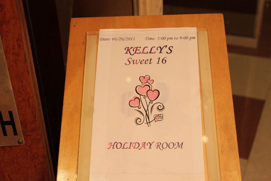 Sign for Kelly's Sweet 16 party at the Holiday Room. Pink hearts logo, date, and time displayed.