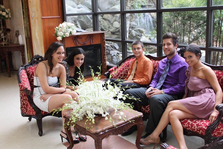 Five people seated on a red patterned sofa near a window, talking. Includes a small table with white flowers.