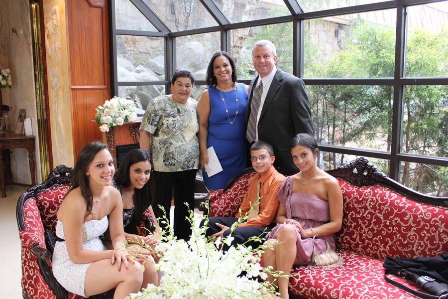 Family posing for a photo. People seated on a red couch and standing against a glass wall.