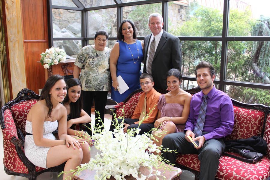 Group of people pose for photo indoors. A floral arrangement sits on a table near a red couch.