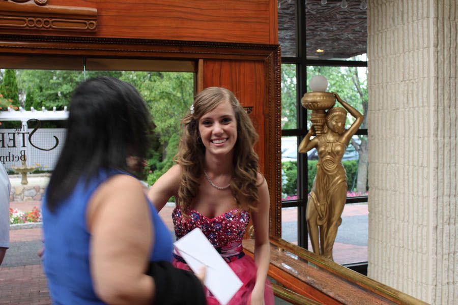 Woman in prom dress smiling, holding a paper, by a golden statue near an entrance.