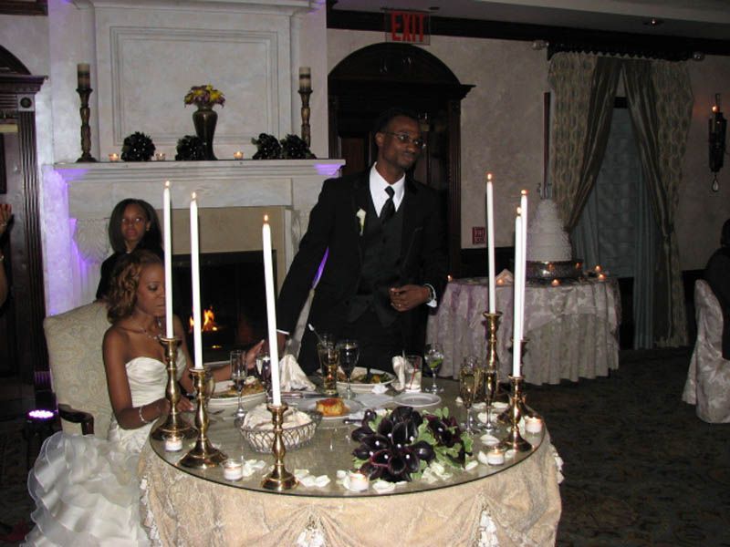 Bride and groom at reception table, lit candles, fireplace, formal attire.