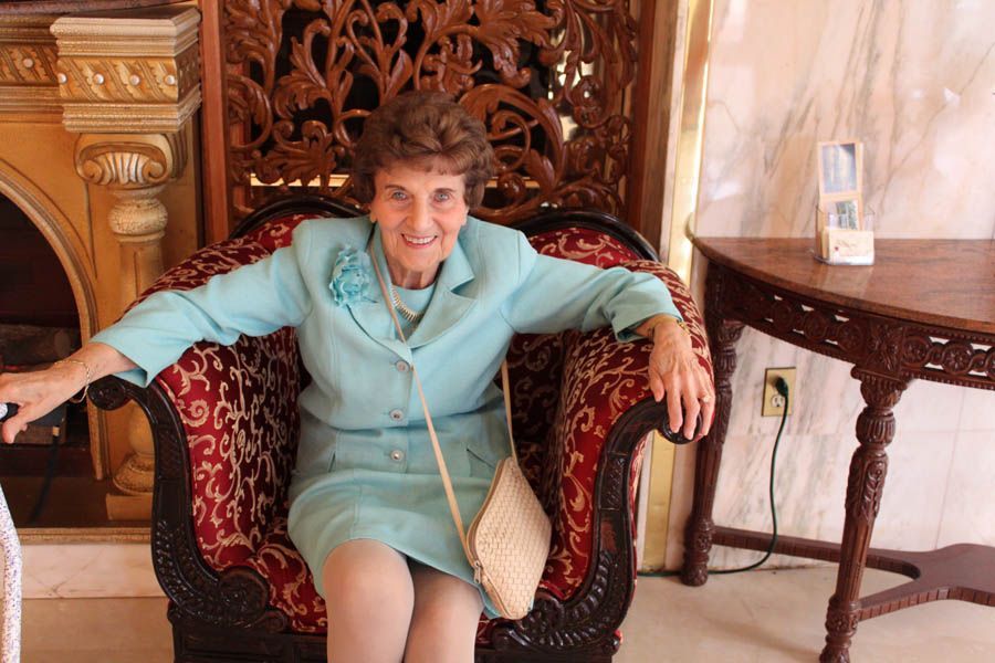 Woman in blue suit seated in ornate chair, smiling.