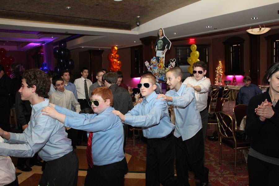 Group of boys in blue shirts and sunglasses, dancing in a ballroom, possibly at a party.