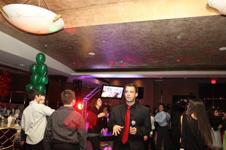People dancing and celebrating at an event. A man in a suit speaks into a microphone.
