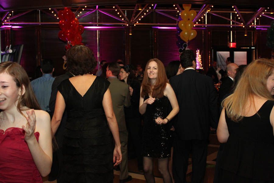 People dancing at a party under purple lights, some wearing formal attire.