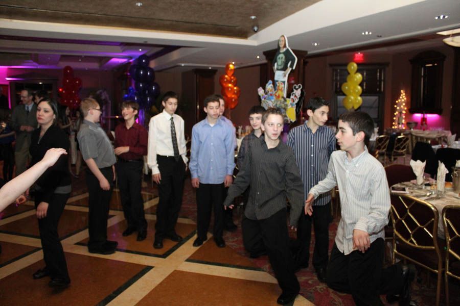 Group of boys at a party, some wearing dress shirts and black pants. Balloons decorate the room.