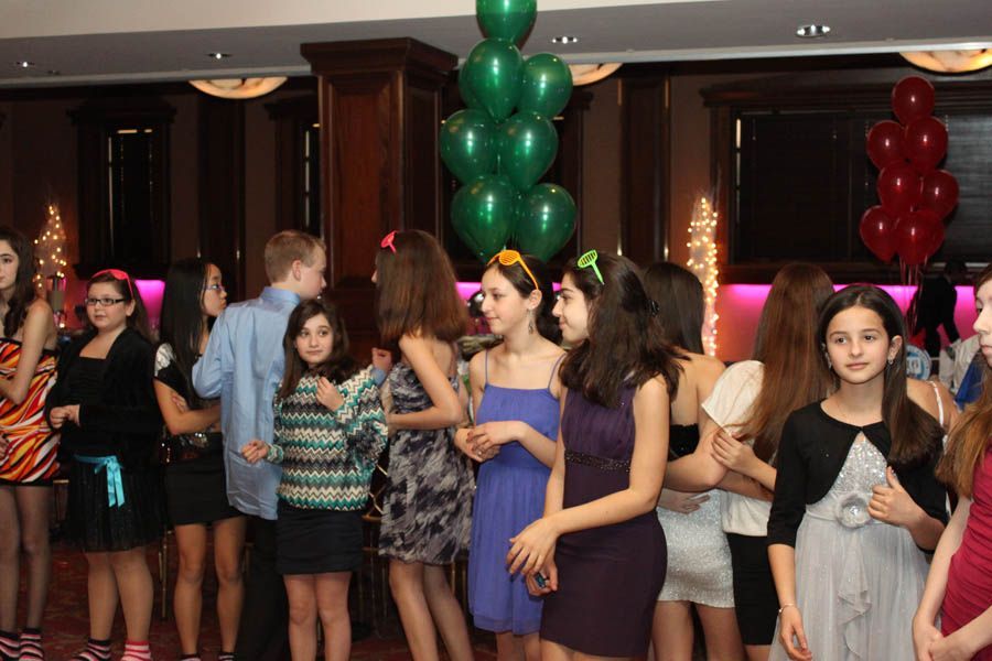 Teenagers at a party, dressed in semi-formal attire. Balloons in green and red are in the background.