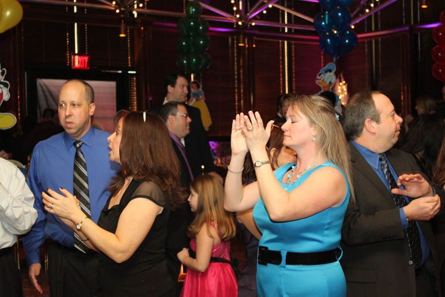 People clapping and dancing at a party, inside a room with colorful decorations.