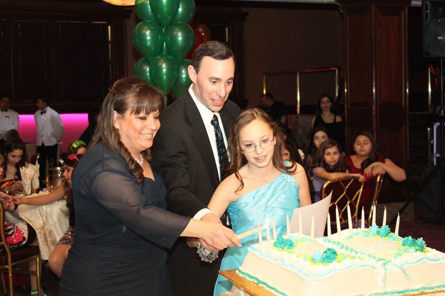 Family cutting birthday cake at a party; balloons in background.