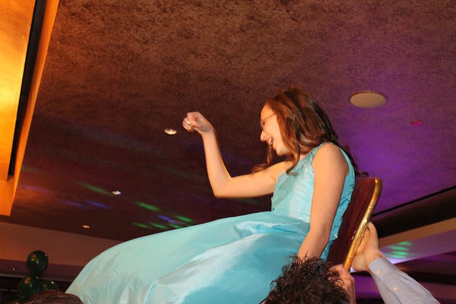 Woman in blue dress sitting on a chair held up by people, celebrating in a party setting.