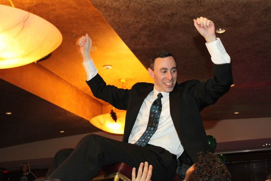 Man in suit raised up, arms in air, smiling in celebration.