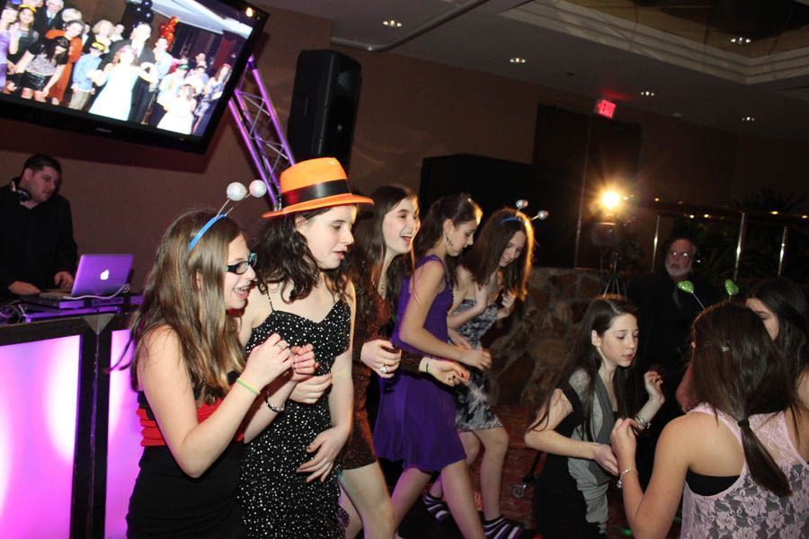 Teenagers dancing at a party, DJ in background, disco lights, one person wearing a hat.
