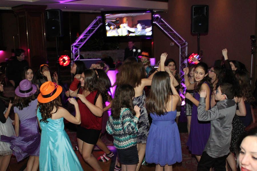 Teens dancing at a party under colorful lights and a TV screen.