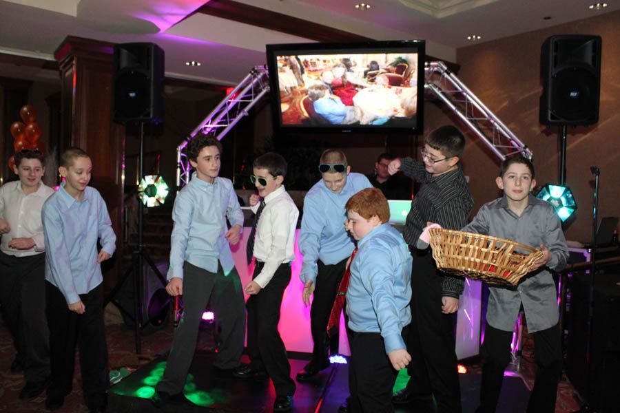 Boys dancing at a party with a large screen, disco lights, and a DJ booth.