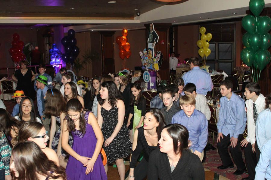 Party with many people dancing, colorful balloons, and festive decorations inside a room.