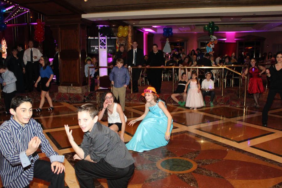 Kids dancing at a party in a large room with balloons.
