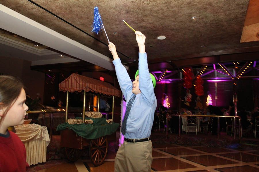 Man in blue shirt with arms raised, holding a wand and flag, in a decorated room with a girl looking on.