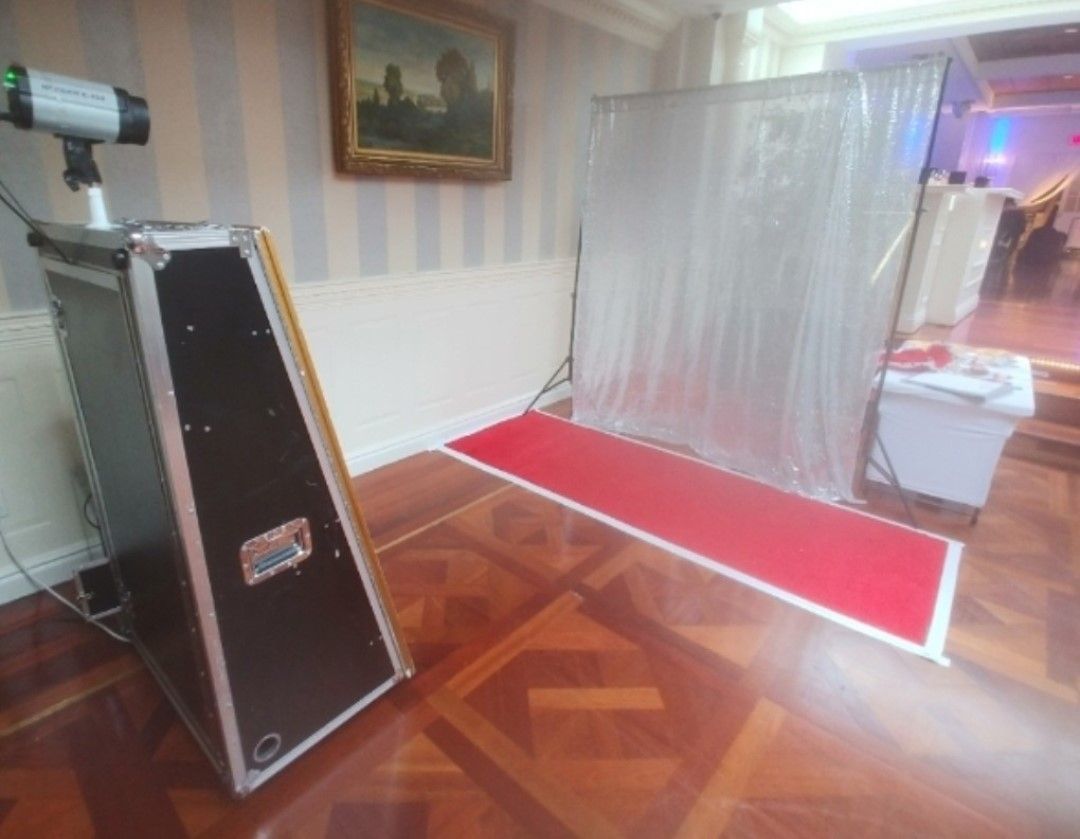 Photo booth setup in a room with a red carpet. The booth has a camera, lights, and a silver backdrop.