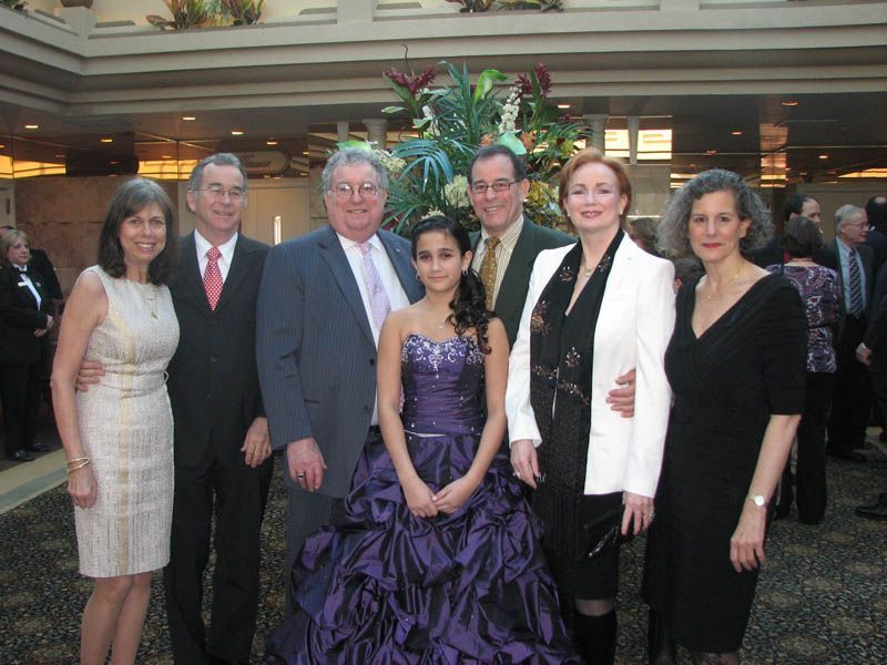 Group of seven people posing for a photo in a formal setting, including a person in a purple gown.
