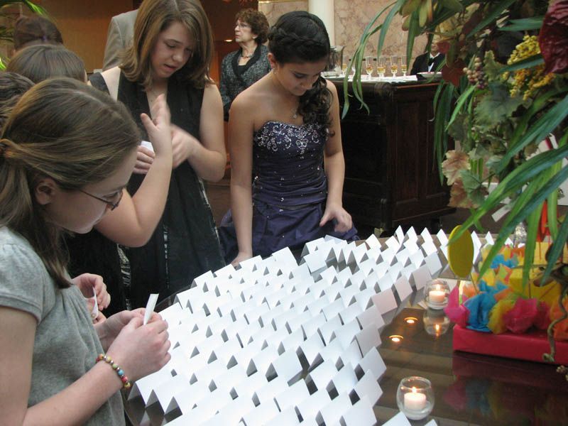 People gathered around a table with a white paper structure, possibly at an event.