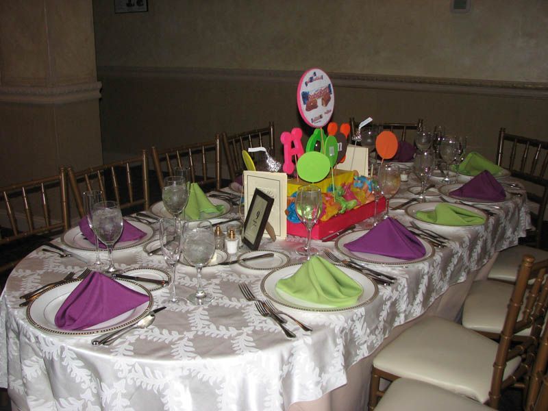 Festive table setting with purple and green napkins, centerpiece with colorful letters.