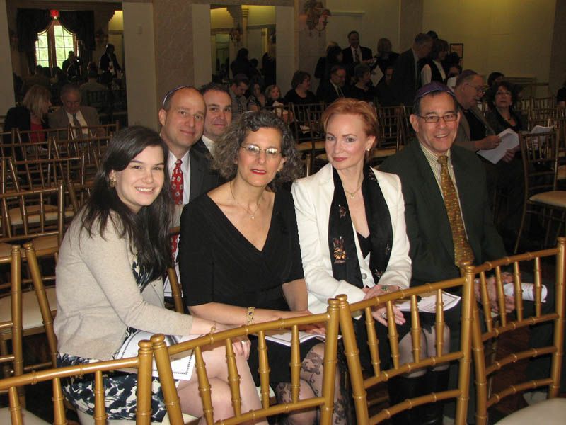 People seated in gold chairs at an event; woman with red hair and others smiling.
