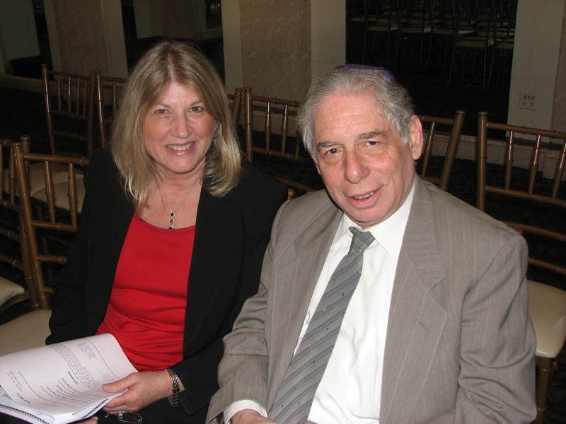 Woman in red top and man in suit smiling, seated indoors.