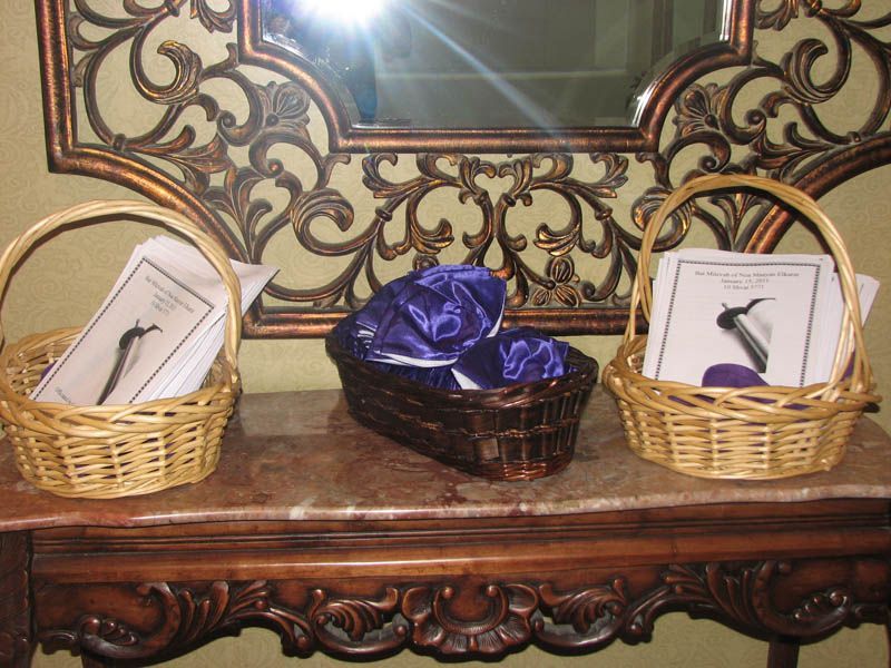 Three wicker baskets on a table under a decorative mirror. Two baskets hold papers, the center holds purple caps.