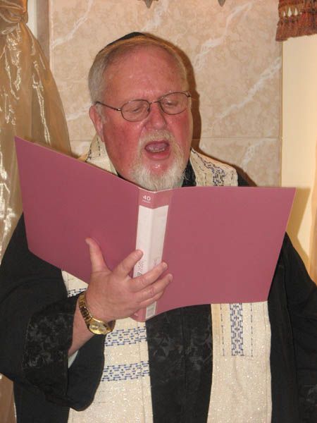 Man in religious garb sings from an open book, indoors.