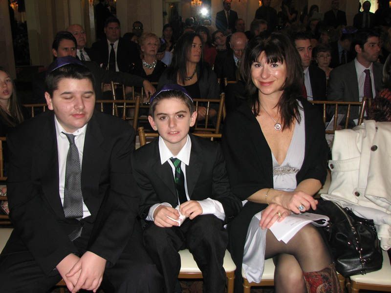 Family, two boys and a woman, seated, dressed formally, at an event.