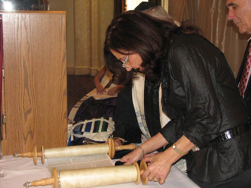 Woman unrolls Torah scroll at a religious ceremony. Wooden cabinet, interior setting.