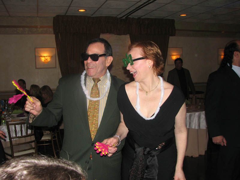 A man and woman dance, wearing sunglasses and party favors, at a party.