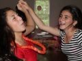 Two women smiling; one in striped shirt, reaching up, the other in red shirt with lei. Indoors.