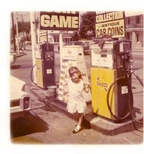 A little girl is standing in front of a gas pump at a gas station.