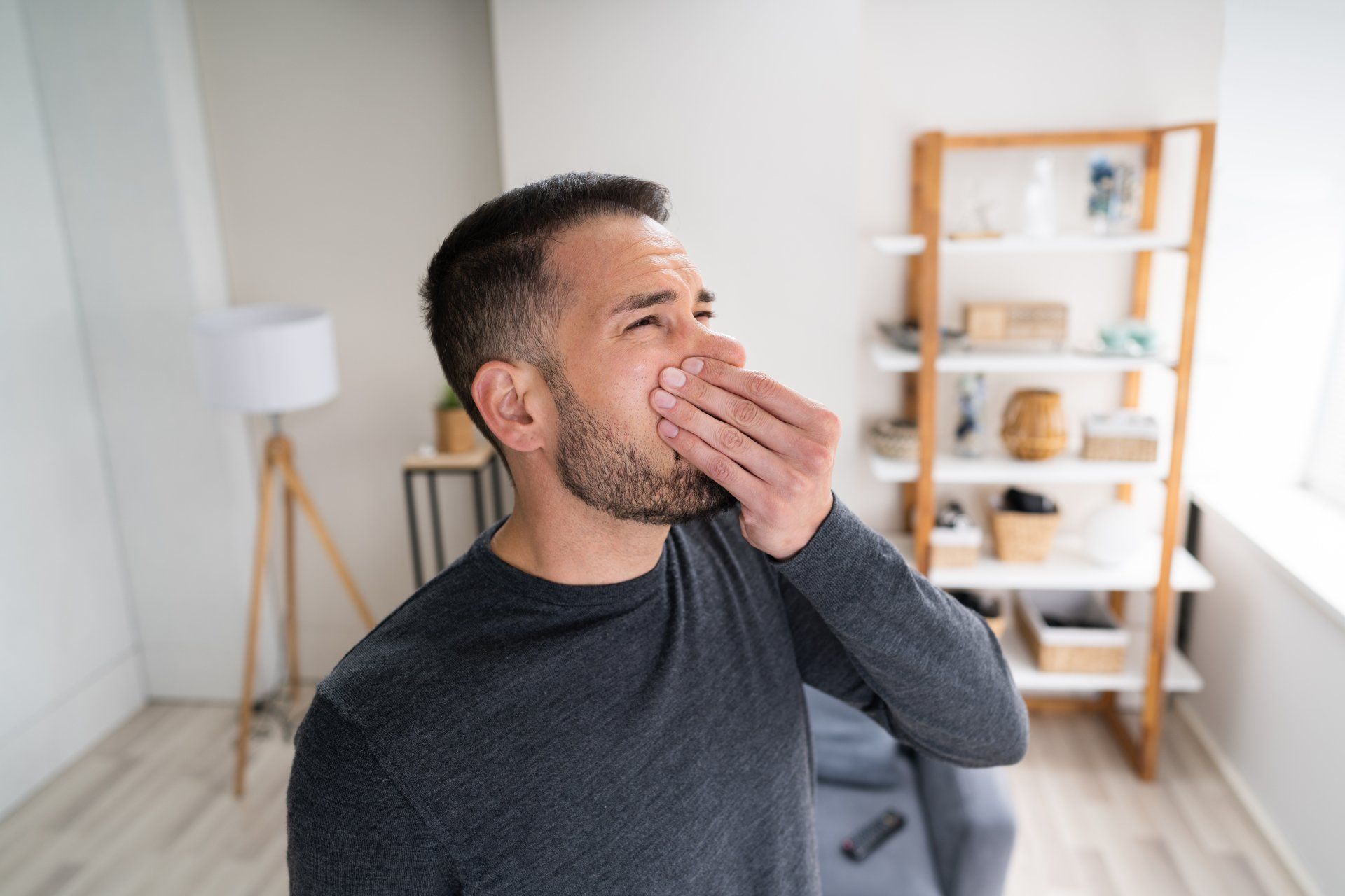 A man is covering his mouth with his hand in a living room. A man is covering his mouth with his hand in a living room.