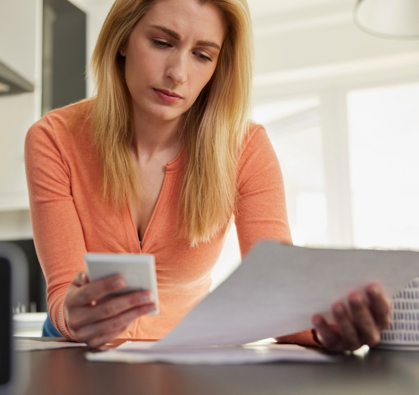 A woman is sitting at a table looking at papers and a cell phone.