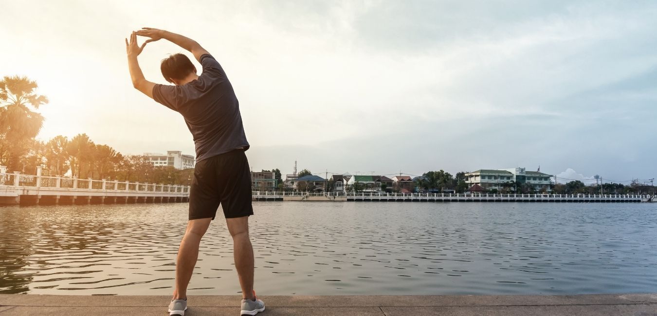 Man stretches near a lake at sunset.