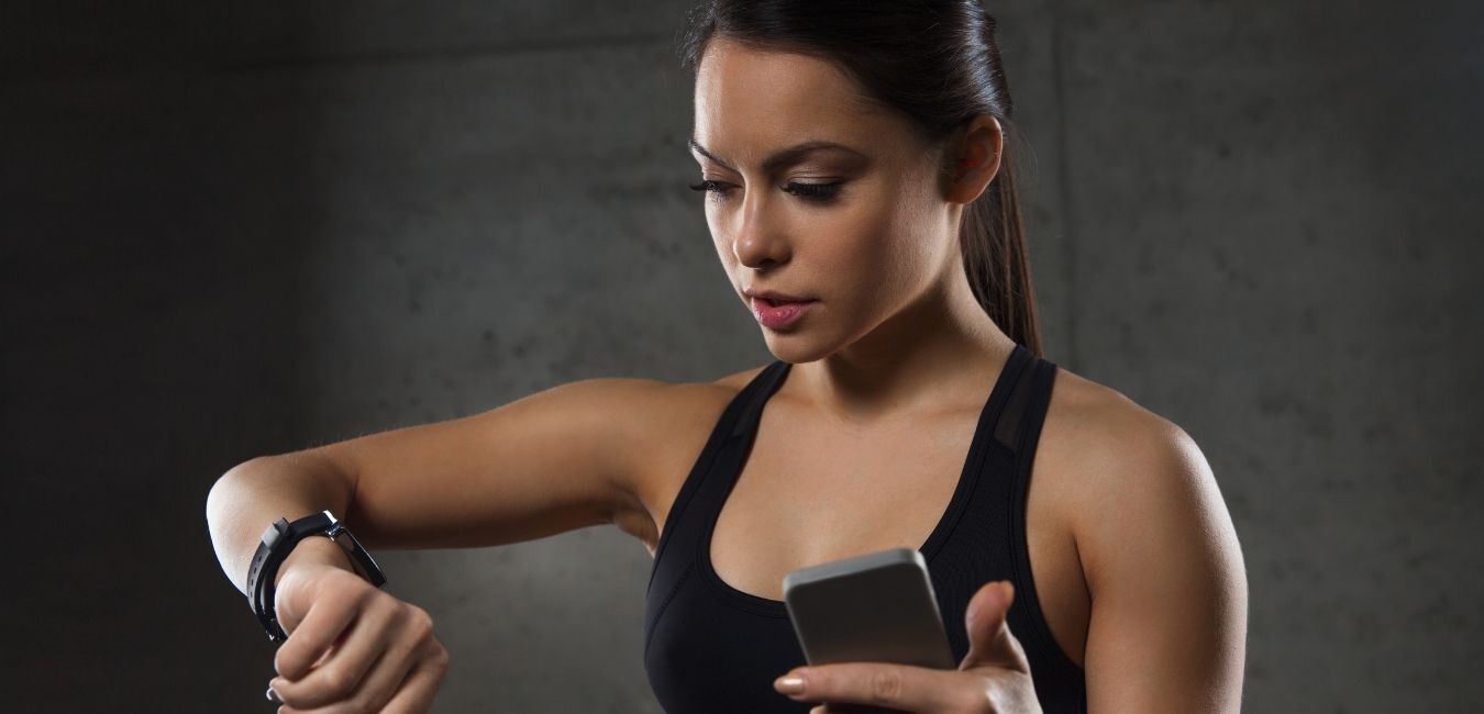Woman in workout clothes looking at smartwatch and phone.