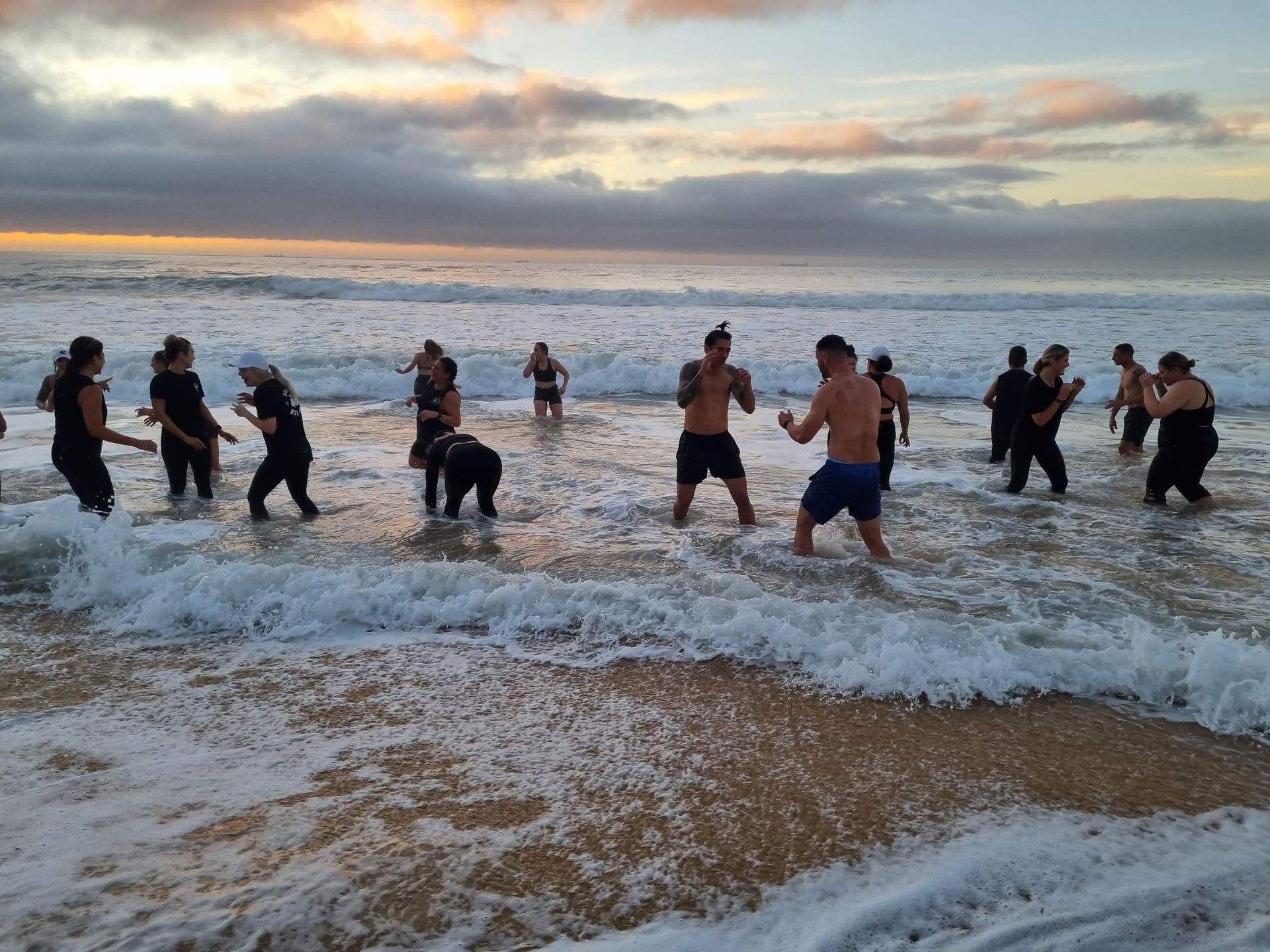 Group exercising in ocean surf at sunset. People are shadow boxing in the water.